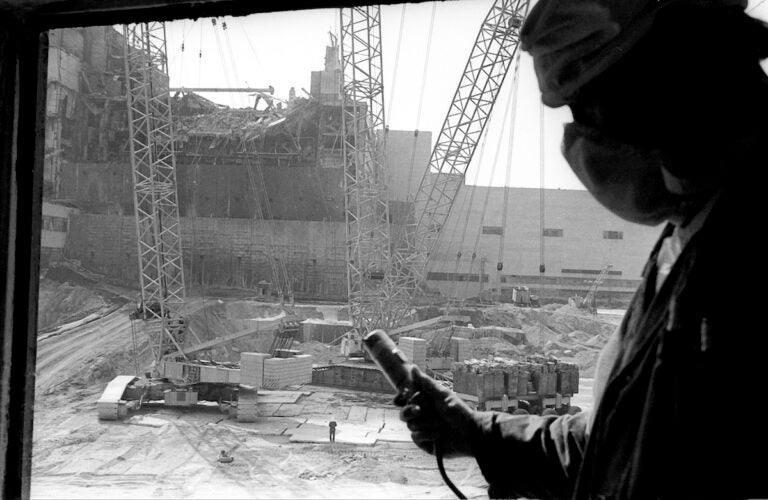 In this 1986 photo, a Chernobyl nuclear power plant worker holding a dosimeter to measure radiation level is seen against the background of a sarcophagus under construction over the 4th destroyed reactor, Ukraine.
