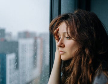 A woman with brown hair looks sadly out of a window