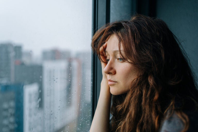 A woman with brown hair looks sadly out of a window