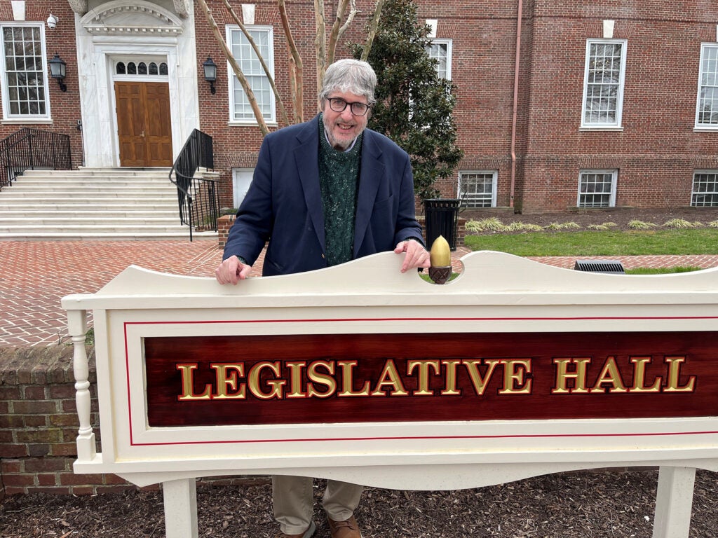 John Flaherty is posing for a photo behind the sign for Legislative Hall.