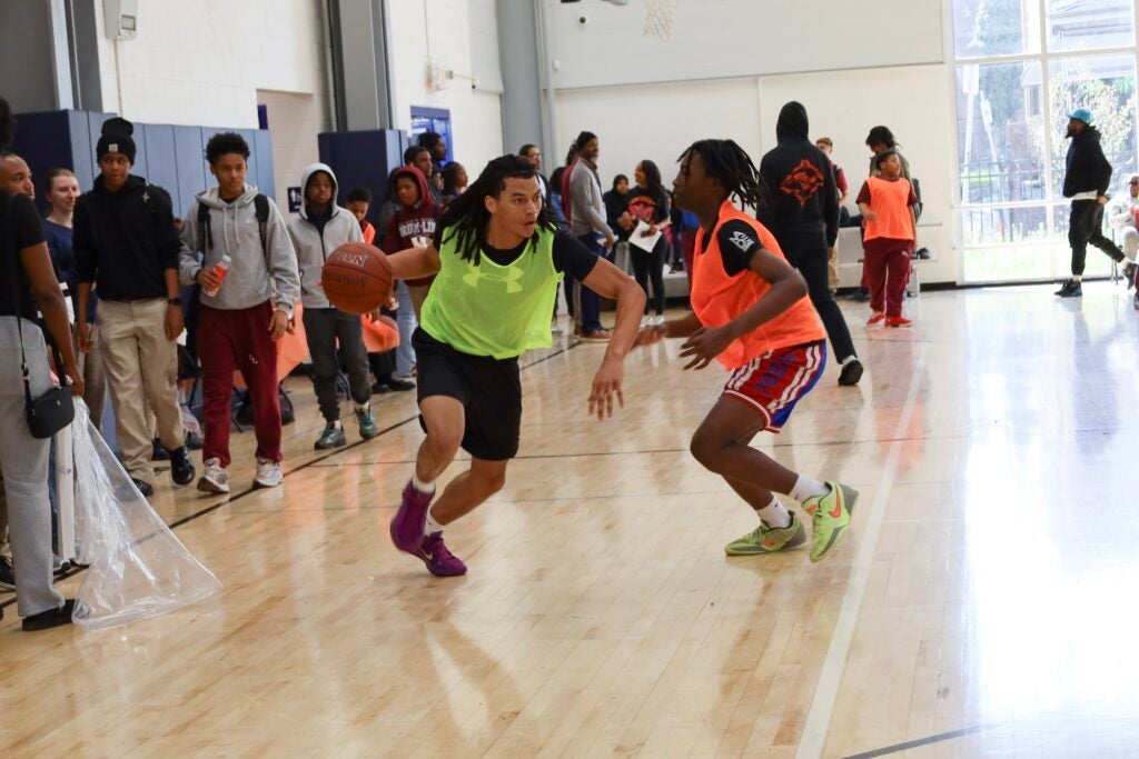 One student drives to the basket with another student defending them.