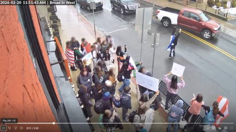 Surveillance photo of protesters blocking an entire sidewalk and one person in the middle of the street.