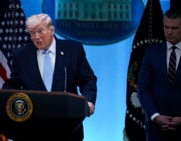 Donald Trump speaking at a podium, with Pete Hegseth standing beside him.