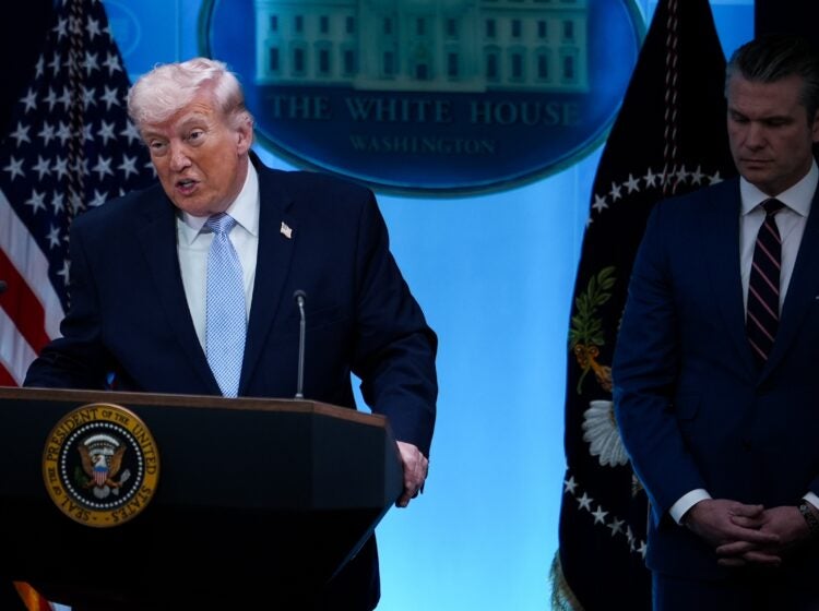 Donald Trump speaking at a podium, with Pete Hegseth standing beside him.