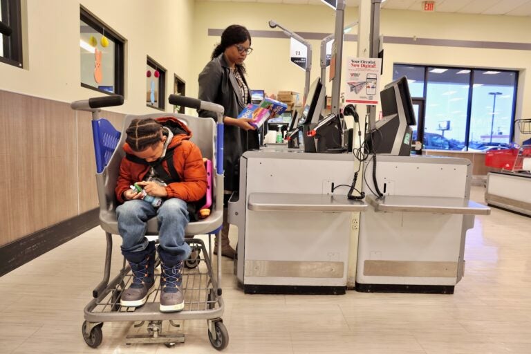Constance Jones scans her purchases while her son, Austen, sits comfortably in a Caroline's Cart