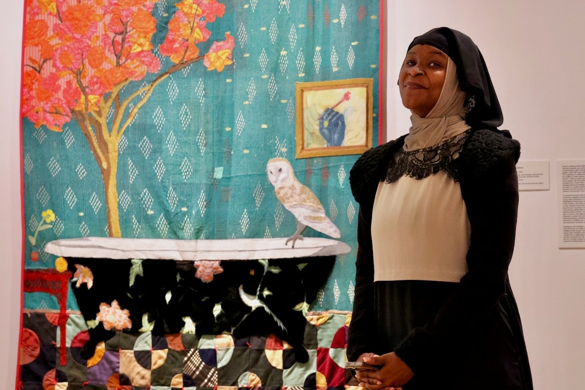 December Collins poses for photo in front of quilts at the Fabric Workshop exhibit