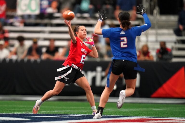 A defender rushing the quarterback who is throwing the ball in a girls flag football game.