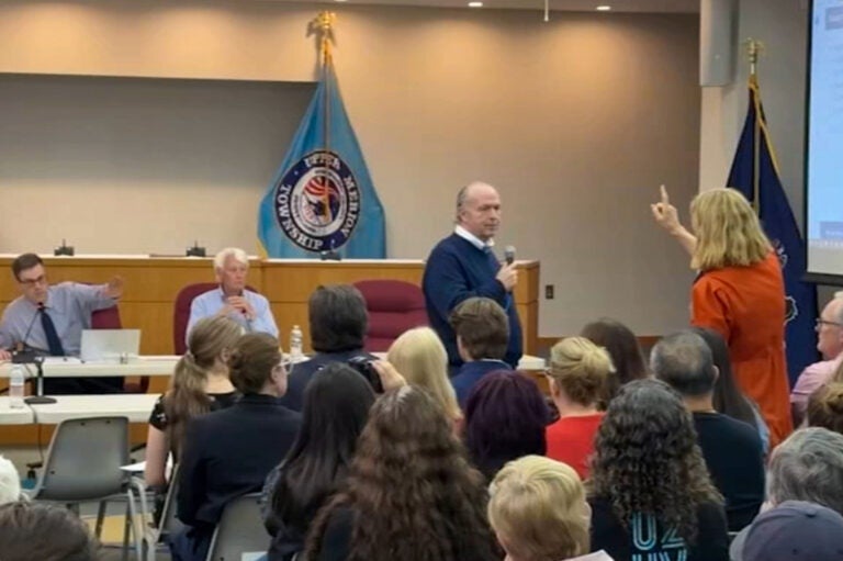 A woman speaking and pointing at panelists sitting at a table during the meeting.