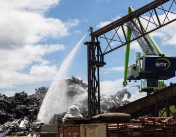 A large crane shoots water down at a pile of scrap metal.