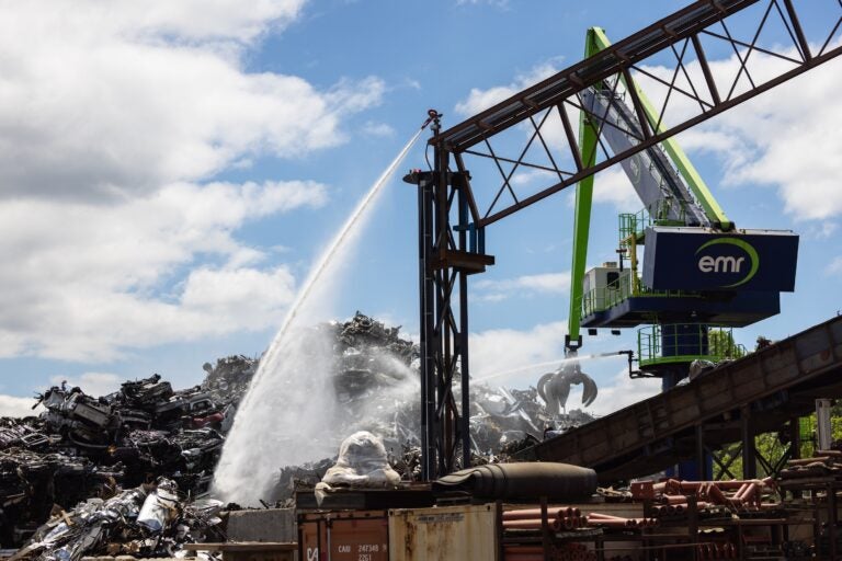 A large crane shoots water down at a pile of scrap metal.