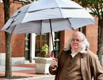A Benjamin Franklin impersonator uses an umbrella to stay out of the sun in Philadelphia's Old City neighborhood on Tuesday, June 30, 2026.