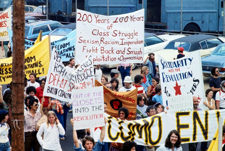 A group of people hold various signs about class struggles during a protest in 1976.