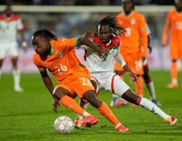 Yan Diomande dribbles the ball while Issa Kabore challenges from behind during a match.