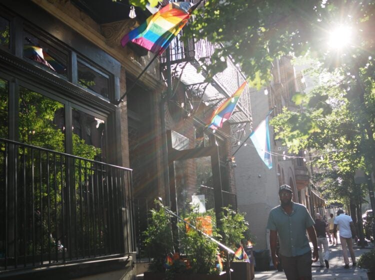 gayborhood-h-kwon-bp-2026-06-16-1 Pride flags hang from apartment buildings on a city street.
