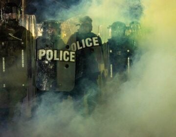 Police in riot gear are seen through the mist at the protewt