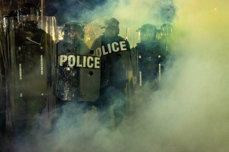 Police in riot gear are seen through the mist at the protewt