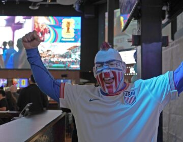A man cheers in a bar with face paint of the American flag
