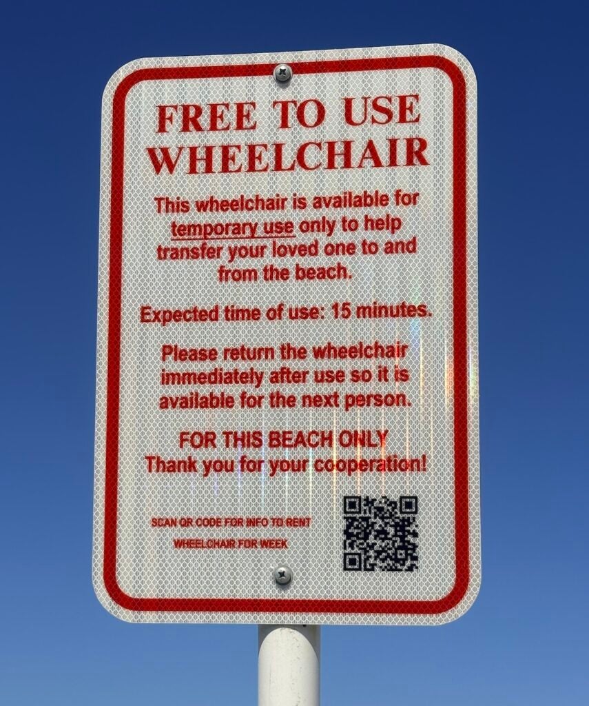 A sign posted at the beach advertises a free to use wheelchair.