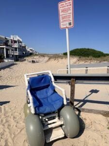 A blue wheel chair with oversized wheels is sitting on the beach, available for use.