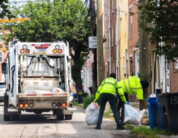 Sanitation workers load bags of trash into the back of the truck.