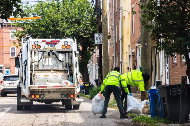 Sanitation workers load bags of trash into the back of the truck.