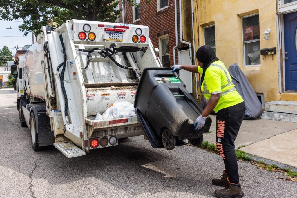 Sanitation workers load bags of trash into the back of the truck.