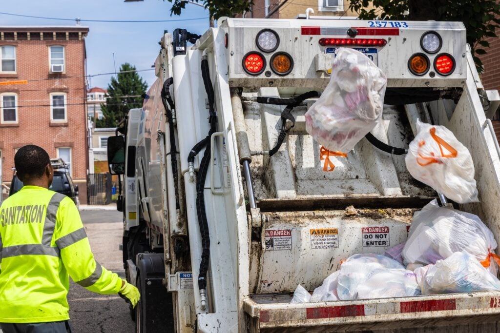 Sanitation workers load bags of trash into the back of the truck.