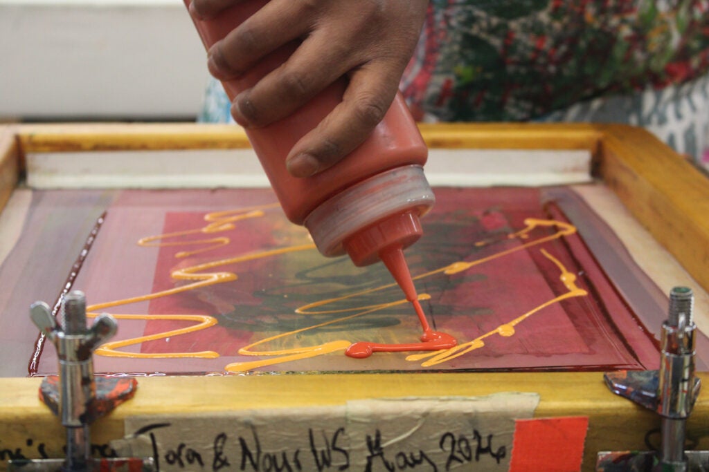 A hand squeezes paint through a bottle onto a canvas