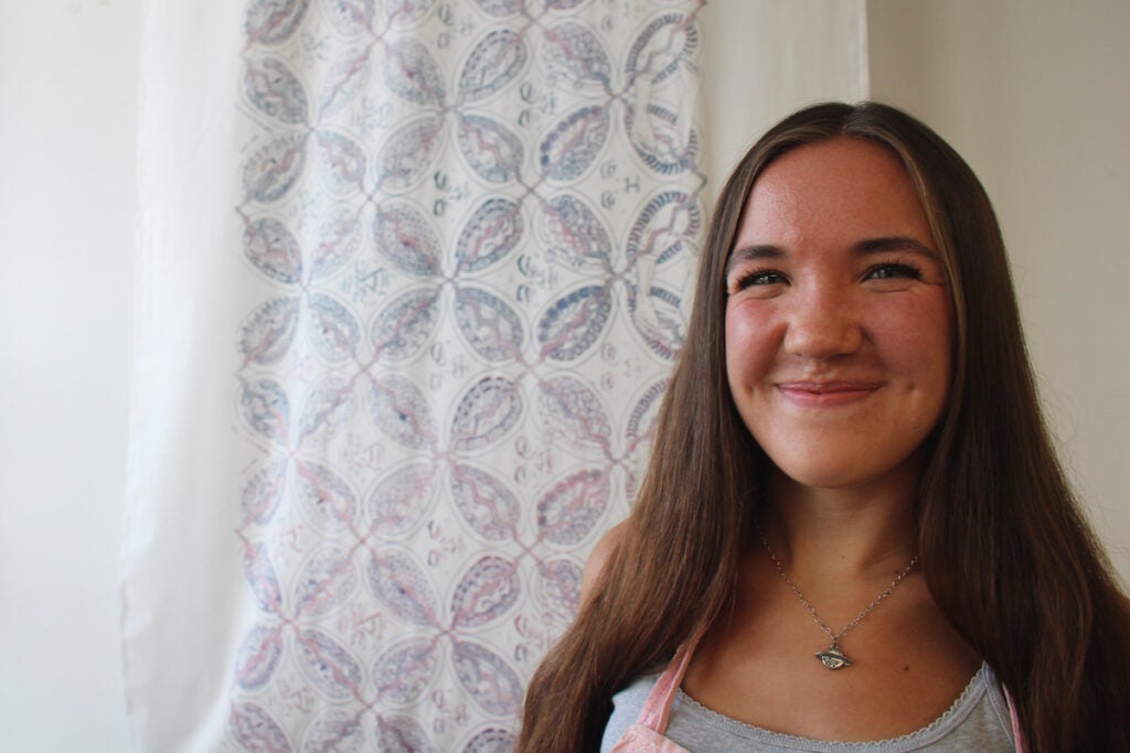 A 17-year-old girl smiles at the camera with her screen-printing project behind her