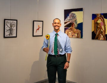 juan-santos-delaware-exhibition-becoming Dominican-born Delaware artist Juan Santos stands in front of his paintings holding a yellow flower