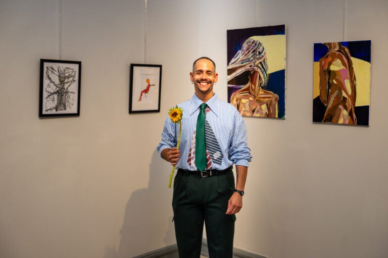 Dominican-born Delaware artist Juan Santos stands in front of his paintings holding a yellow flower