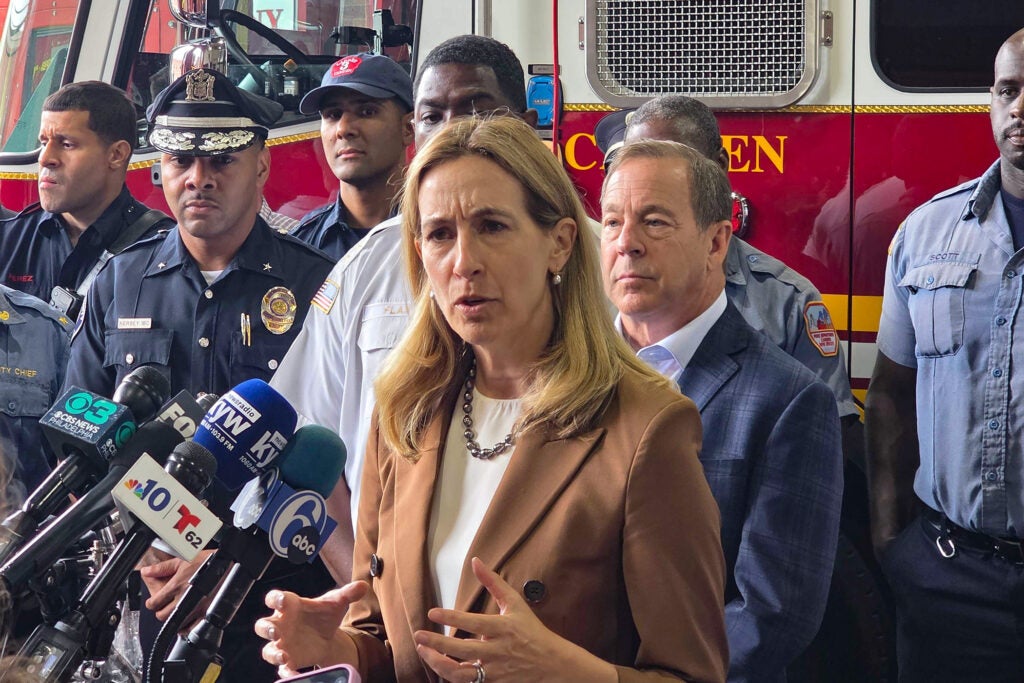Mikie Sherrill at a podium addressing the media surrounded by police and fire officials.