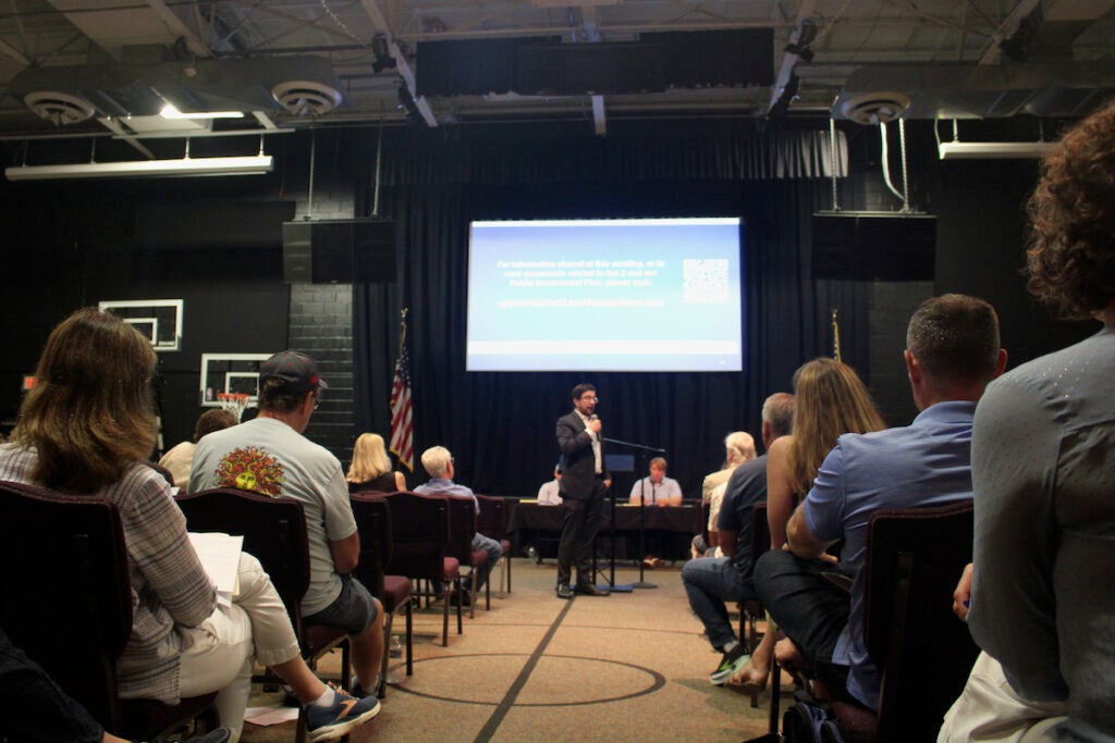 Ben Weldon is speaking into a microphone during the town hall meeting.