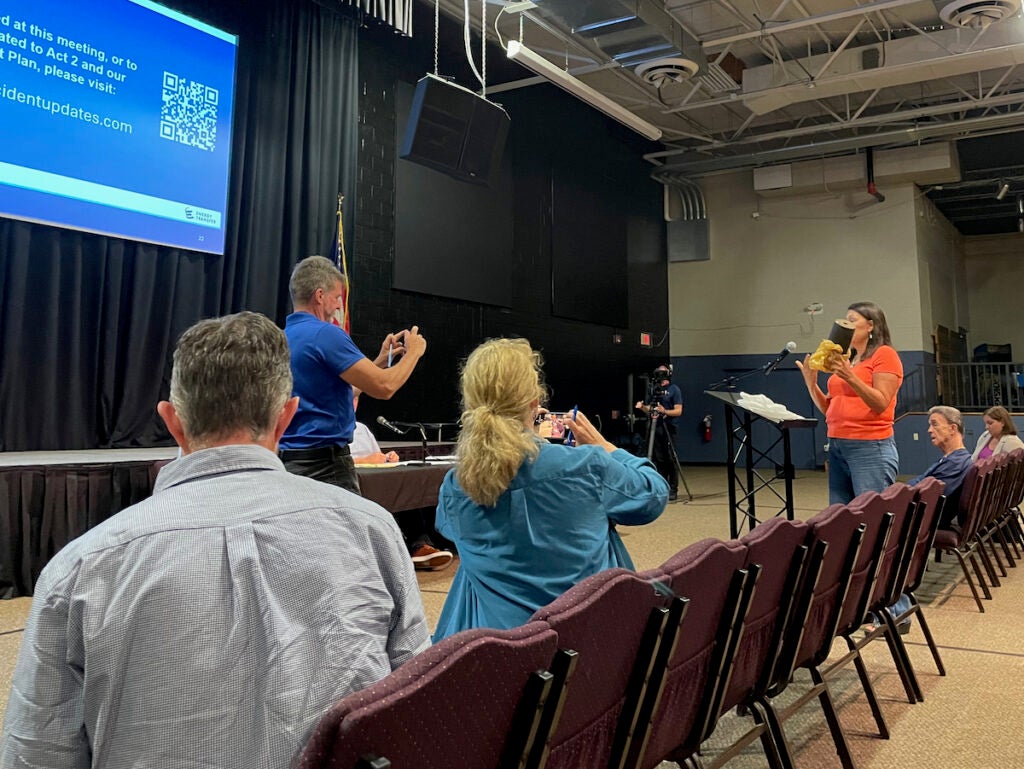 Kim Brunnquell is addressing the panelists during the town hall meeting at a microphone in the audience.