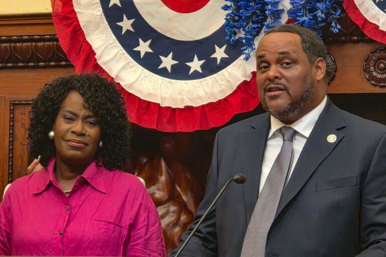 Carlton Williams speaking at a podium in City Hall, with Mayor Cherelle Parker standing beside him.