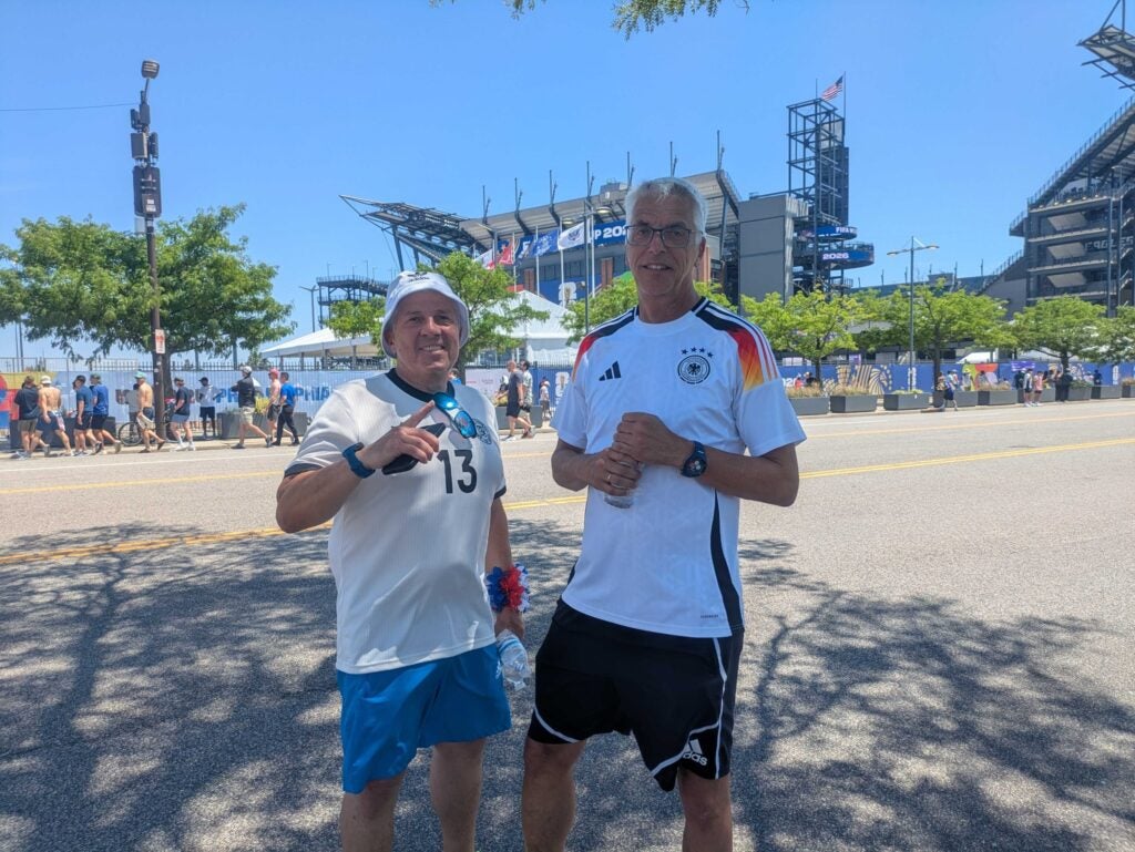 Two men wearing Germany jerseys in the parking lot heading into the stadium for the World Cup match.