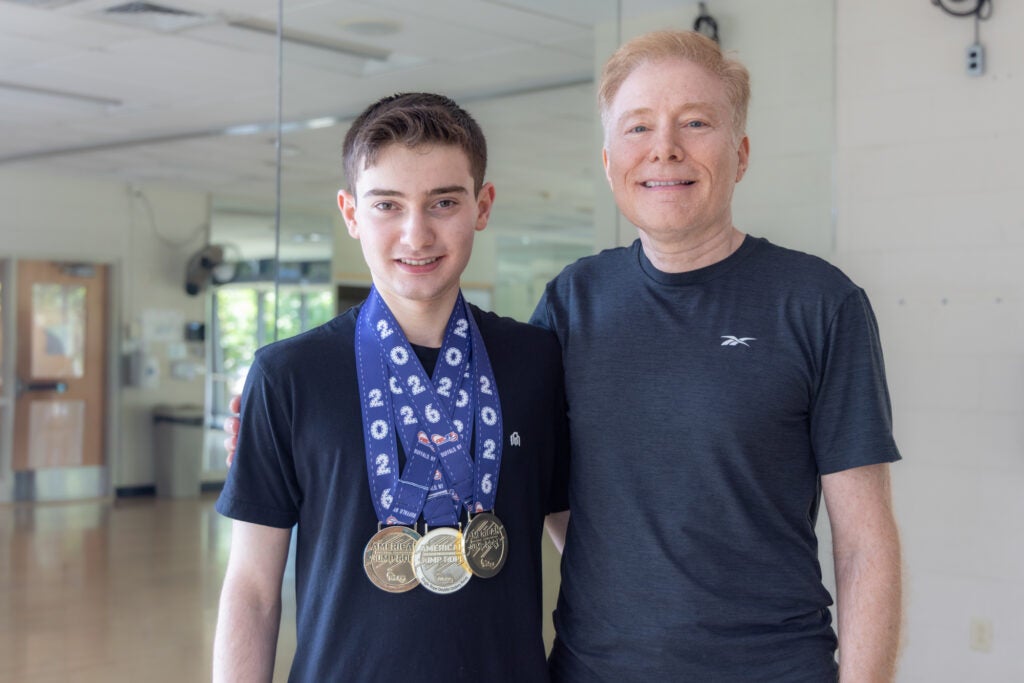 17-year-old Zach Peckman poses for a photo with his father Marcus in the YMCA. Zach has 3 medals hanging around his neck.