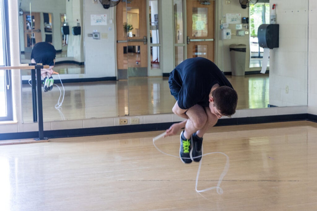 Zach Peckman is in mid-air as he is jumping rope. He is hunched far forward, with his arms beneath his legs as he does a trick with the rope inside the YMCA in Doylestown, Pa.