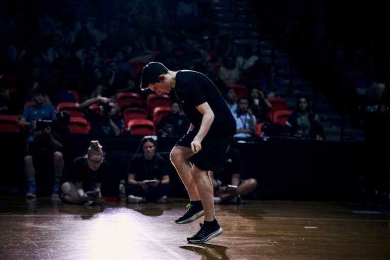 Zach Peckman is jumping rope at the competition in Buffalo, NY. He is hunched forward and is whipping the rope so quickly it is barely visible. A crowd of onlookers watch.