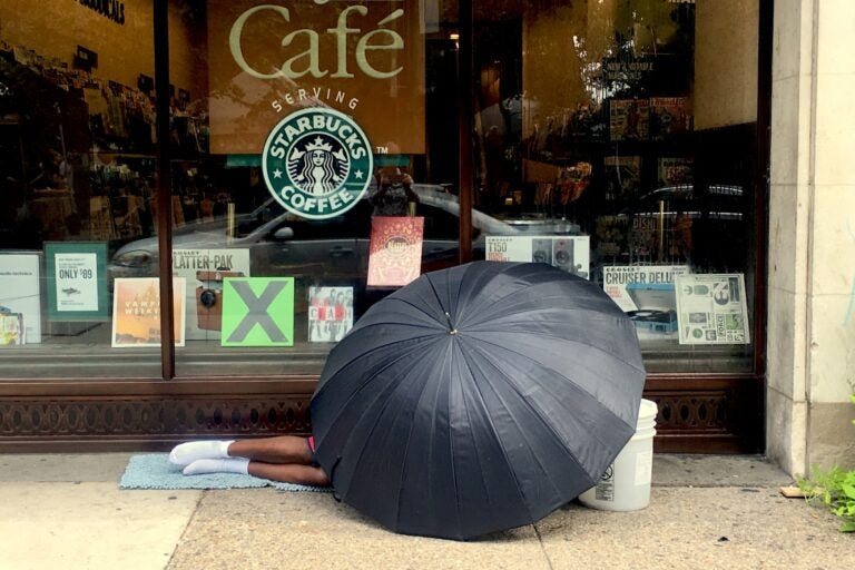 a person sleeping on the sidewalk, under an umbrella