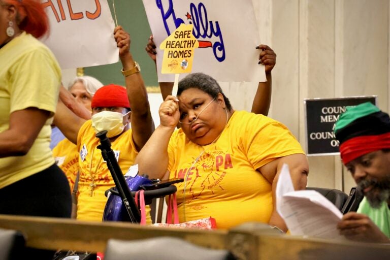 Melissa Monts attends a Philadelphia City Council meeting and holds a sign reading SAFE HEALTHY HOMES