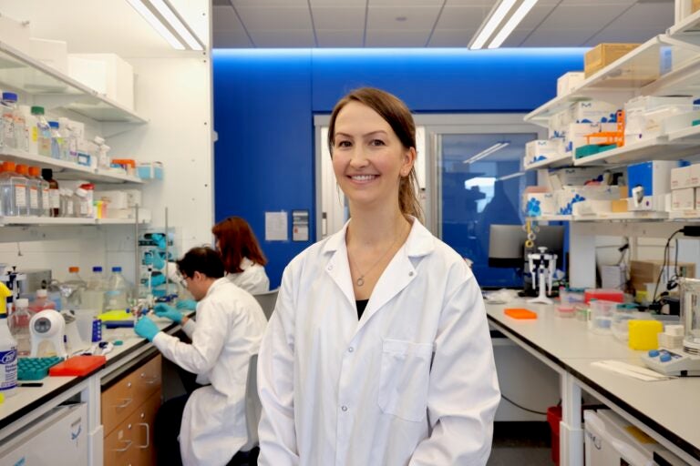 Brittney Allyn is in her busy lab at University of Pennsylvania. Two researchers are working together at at table behind her.