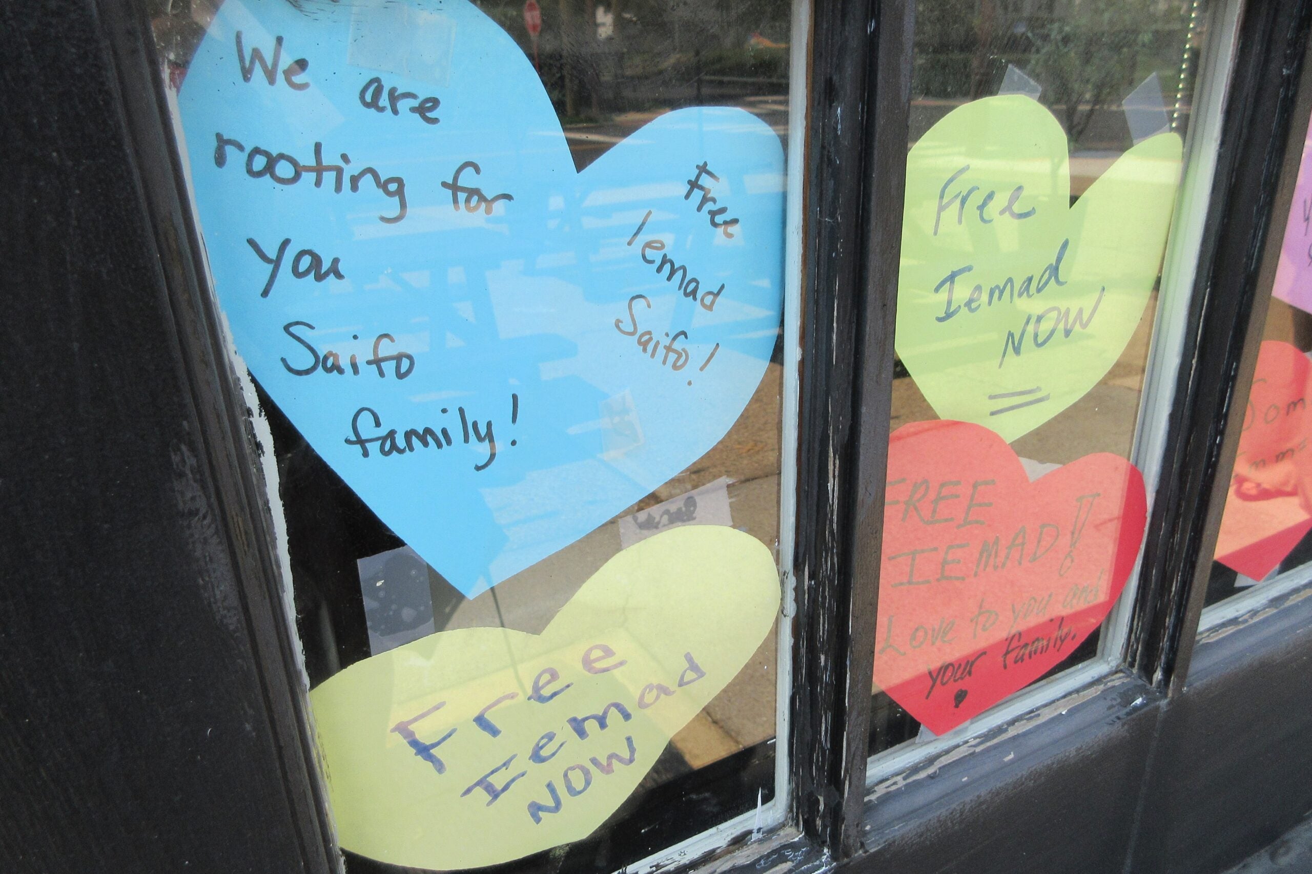 Heart-shaped notes on a restaurant window read We are rooting for you Saifo family! Free Iemad Saifo! and Free Iemad NOW and FREE IEMAD! Love to you and your family.