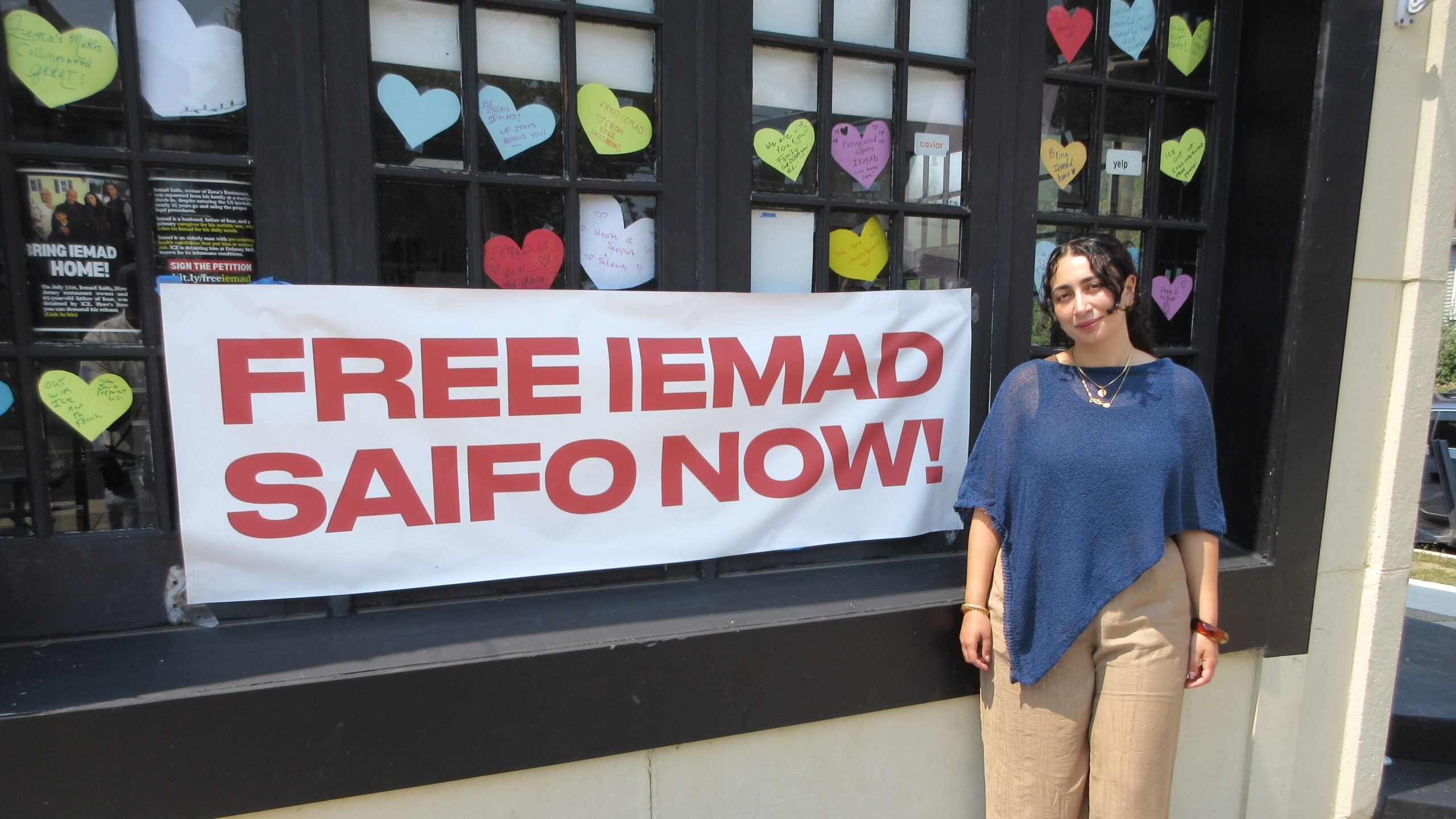 Zena Saifo stands in front of the restaurant named for her, with a sigh that reads FREE IEMAD SAIFO NOW!