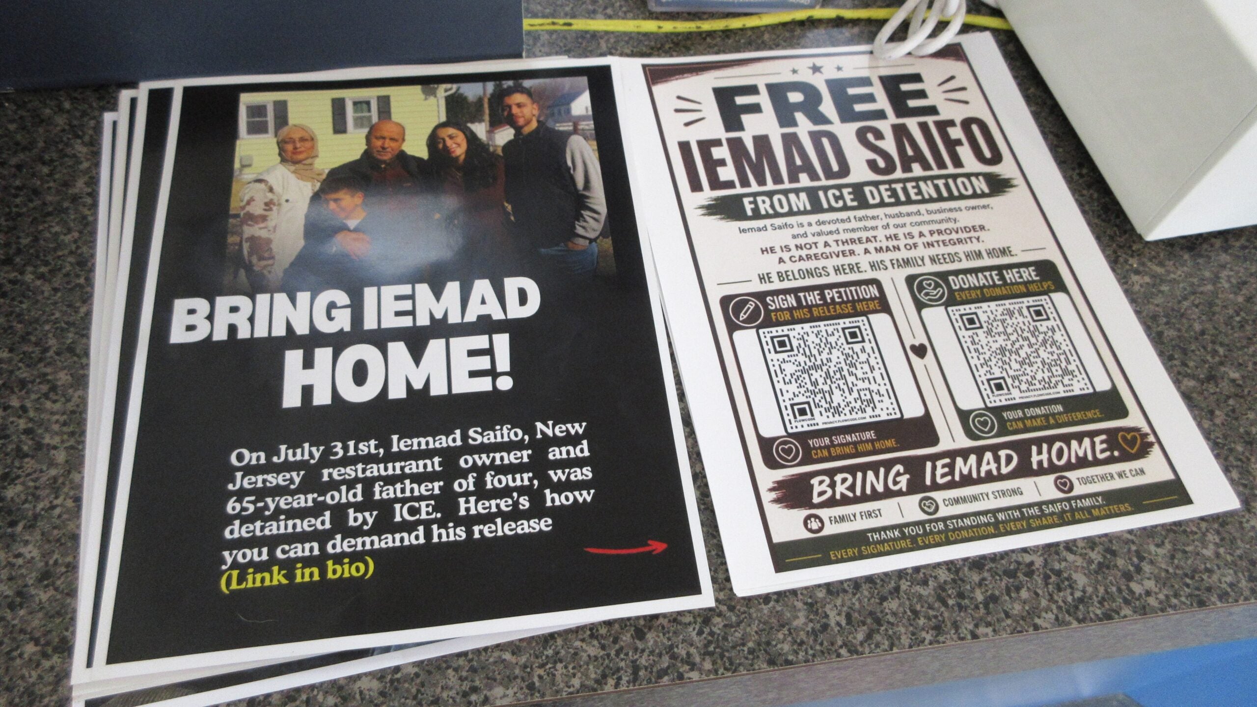 one stack of fliers reads BRING IEMAD HOME! On July 31st, Iemad Saifo, New Jersey restaurant owner and 65-year-old fathr of four, was detained by ICE. Here's how you can demand his release (Link in bio). Another stack reads FREE IEMAD SAIFO FROM ICE DETENTION Iemad Saifo is a devoted father, husband, business owner, and valued member of the community. HE IS NOT A THREAT. HE IS A PROVIDER. A CAREGIVER. A MAN OF INTEGRITY. HE BELONGS HERE. HIS FAMILY NEEDS HIM HOME.