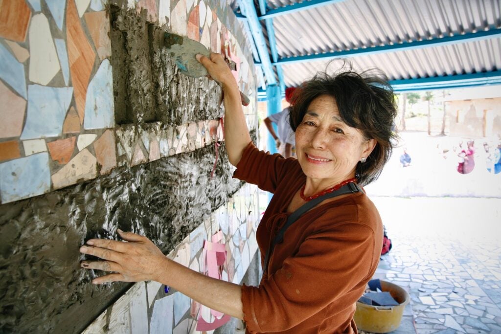 A portrait of the artist, Lily Yeh, taken in 2007, posing near a wall with mosaic art