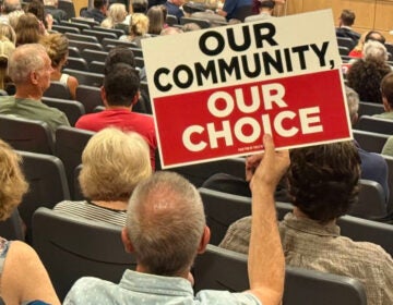 Conshohocken-data-center-zoning-board-meeting-scaled-file People at a town hall, one person holds a sign reading OUR COMMUNITY, OUR CHOICE