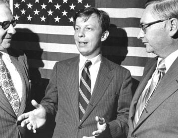Franklin-Kury-PaHouseArchives-1 Franklin Kury speaking with 2 other men while standing in front of a large American flag.