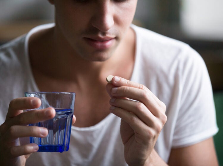 A person prepares to take a medication while holding a glass of qater