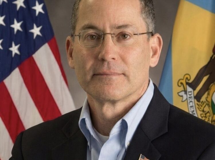Michael Katz headshot, standing in front of an American flag, and a Delaware state flag.